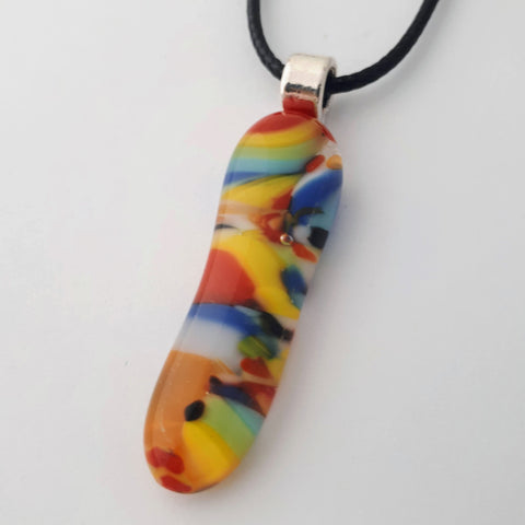 Long oval glass fused necklace pendant with colourful orange, blue, red, yellow, with small bits of green and white chunks/specs in it, with silver coloured bail and black cord on white background