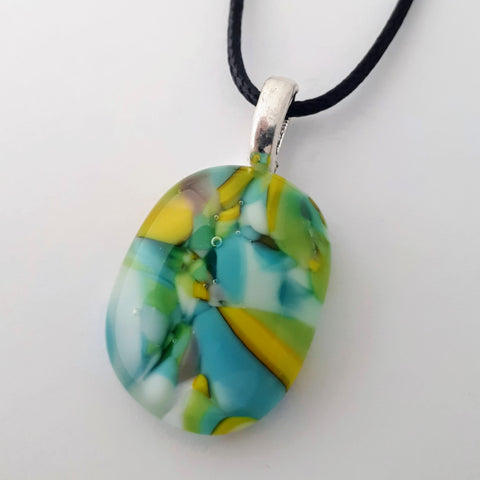 vertical oval glass fused necklace pendant with colourful blue, yellow, green and white chunks/specs in it, with silver coloured bail and black cord on white background