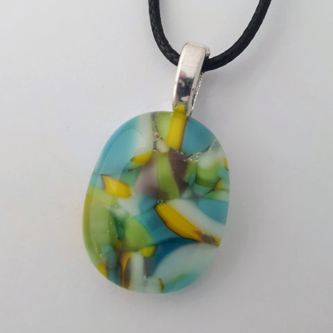 vertical oval glass fused necklace pendant with colourful blue, yellow, green and white chunks/specs in it, with silver coloured bail and black cord on white background