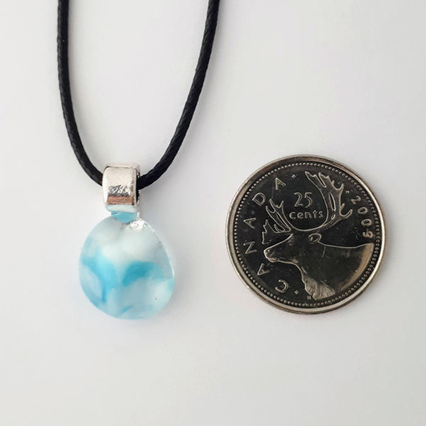 small blue and white oblong glass pendant with silver coloured bail and black cord on white background with quarter for scale