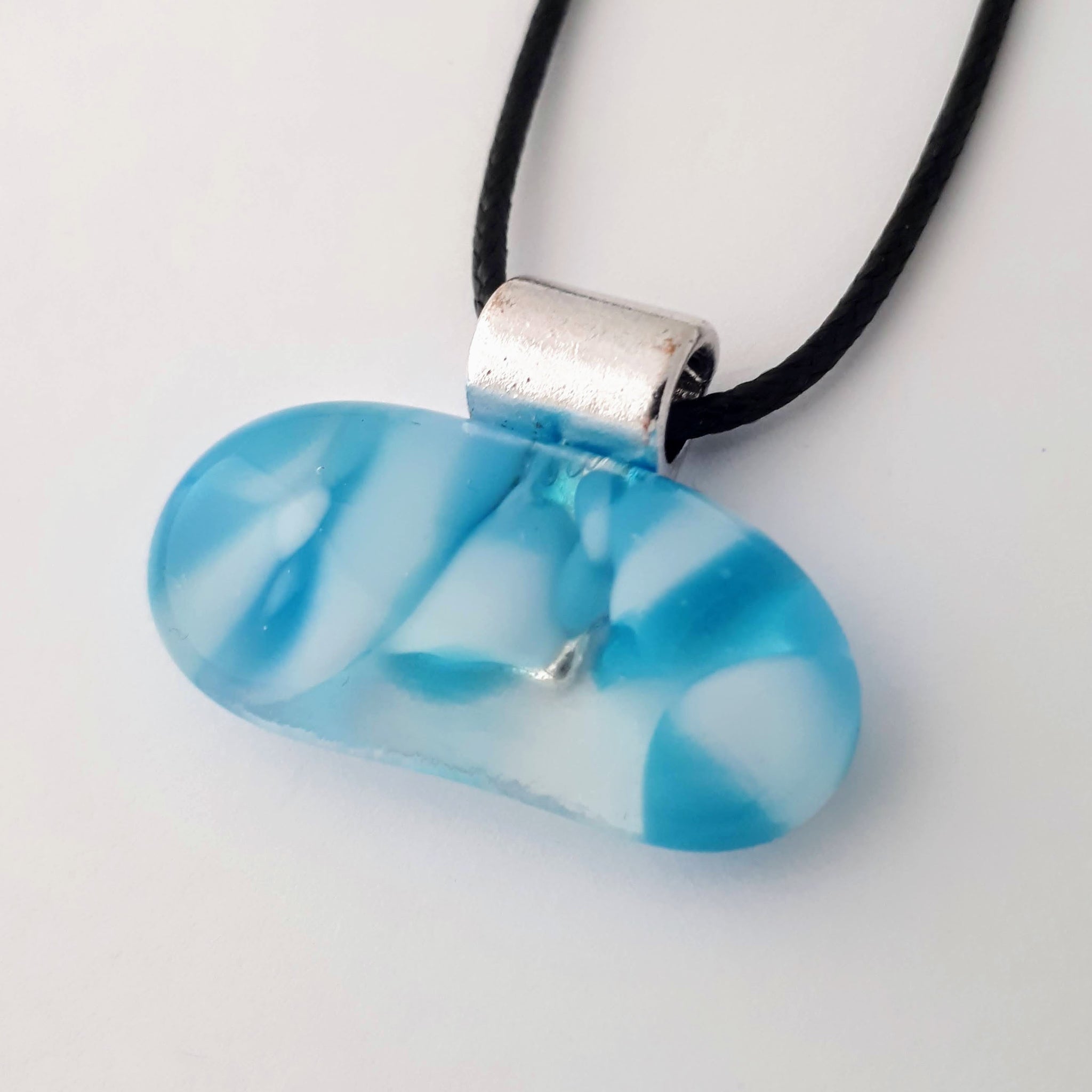 Blue and white wide oval/kidney shaped glass fused pendant with silver coloured bail and black cord on white background