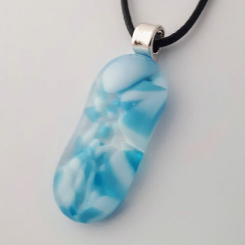 Blue and white glass fused pendant, long oval, with silver bail and black cord on white background
