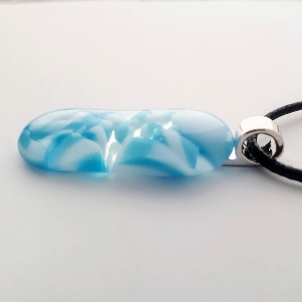 Blue and white glass fused pendant, long oval, with silver bail and black cord on white background side view