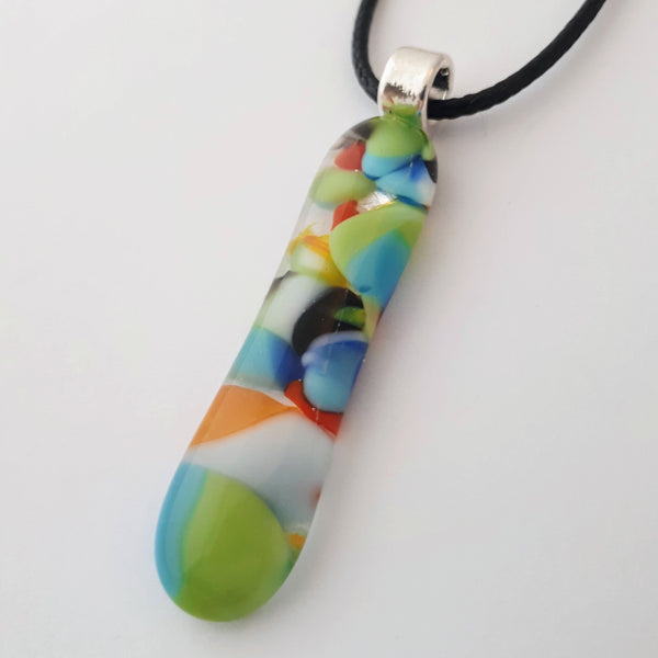 Mainly blue and green multicoloured long skinny glass necklace pendant on white background with black cord and silver coloured bail